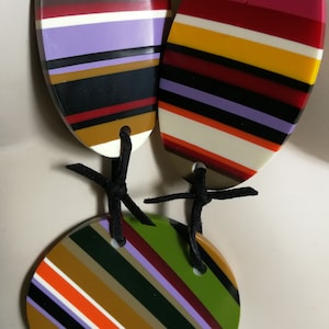 May include: A multi-colored striped necklace with three round and oval pendants. The pendants are made of white, black, red, orange, yellow, green, brown, and purple stripes.