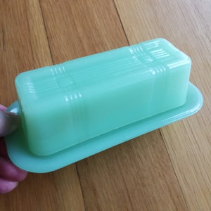May include: A vintage green glass butter dish with a lid. The dish is rectangular in shape and has a smooth, glossy finish.