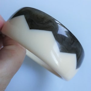 Op de afbeelding: Een witte en zwarte plastic armband met een chevron-patroon.