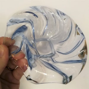 May include: A clear glass bowl with a blue swirl design. The bowl is shaped like a shell and has a small, square opening in the center.
