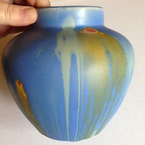 Peut inclure: Un vase en céramique bleu avec un glaçage en gouttes dans des tons de jaune, blanc et vert. Le vase a un corps arrondi et une lèvre légèrement évasée.