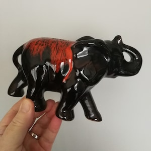 May include: Black ceramic elephant figurine with red and orange glaze. The elephant has its trunk raised and is walking.