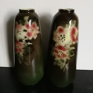 Pode incluir: Dois vasos de cerâmica castanho com um design floral. Os vasos têm um fundo castanho escuro com flores brancas e cor-de-rosa.
