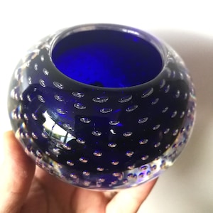 Op de afbeelding: Een ronde, heldere glazen kom met een diepblauwe binnenkant. De buitenkant is bedekt met kleine, gelijkmatig verdeelde luchtbellen. Het licht reflecteert op het glas.