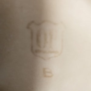 May include: Close-up of a white porcelain mark with a shield-shaped logo containing the letters "GF" and the letter "B" below it.