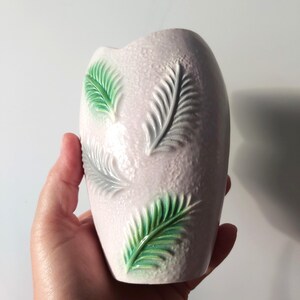 May include: A light pink ceramic vase with a textured surface and embossed green and gray leaf designs. The vase has an oval shape and is approximately 6 inches tall.
