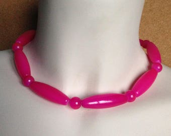 Peut inclure: Un collier rose vif présenté sur un mannequin. Le collier est composé d'une série de perles ovales allongées alternant avec de plus petites perles rondes. Les perles sont d'un rose brillant et uni, créant un accessoire audacieux et accrocheur.