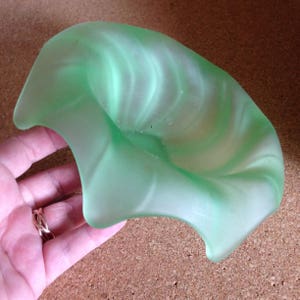 May include: A light green, leaf-shaped glass dish with a swirled, frosted design. The dish has a shallow bowl and three curved edges. The color is a soft, pastel green with white highlights. The dish is likely vintage or antique.