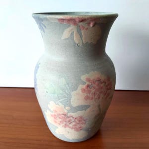 May include: A ceramic vase with a pale blue hue, adorned with floral patterns in pink, white, and green. The vase features a wide opening and a textured finish. Ideal for displaying flowers or as a decorative item.