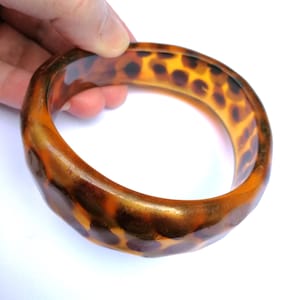 Peut inclure: Un bracelet jonc épais, de forme ovale, avec un motif écaille de tortue. Le bracelet présente un mélange de teintes ambre, marron et noir, avec une finition brillante. Le bracelet mesure environ 6,35 cm de diamètre.