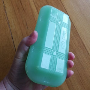 May include: A pale green rectangular dish with a raised geometric pattern and the words "100% CHINA" printed on the side.