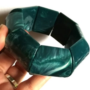 May include: A green and white marbled bracelet made of large, rectangular beads. The bracelet is made of a smooth, polished material.