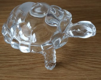 May include: A clear glass turtle ornament with a textured shell, head, and legs. The figurine is on a wooden surface. The turtle's shell has a bubbly texture, and the head and legs are smooth.