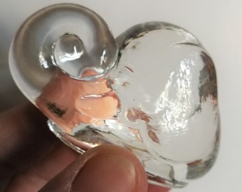 Pode incluir: Uma figura de elefante de vidro transparente com a tromba enrolada. O elefante está deitado com a cabeça apoiada nas patas da frente.