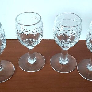 Puede incluir: Cuatro copas de vino de cristal transparente con diseños de diamantes y hojas grabados. Las copas tienen una base redonda, un tallo delgado y una parte superior en forma de cuenco. Están dispuestas sobre una superficie marrón.