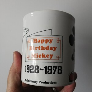K&ouml;nnte beinhalten: Wei&szlig;er Keramikbecher mit schwarzem und orangefarbenem Design. Der Becher tr&auml;gt den Text "Happy Birthday Mickey" und die Jahreszahlen "1928-1978". Er hat auch ein Walt Disney Productions-Logo und eine Mickey Mouse-Illustration.