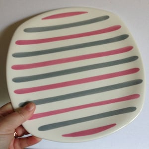 May include: A white oval-shaped serving plate with alternating pink and grey stripes.