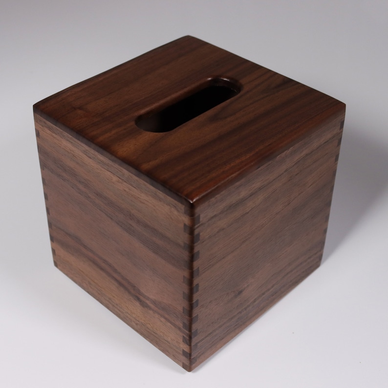 May include: A dark brown wooden tissue box cover with a rectangular opening on the top. The box is made of solid wood with a natural grain pattern.