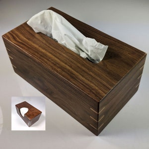 May include: A wooden tissue box cover made of dark walnut wood with a natural wood grain pattern. The box has a rectangular shape with a slot for tissues on the top.