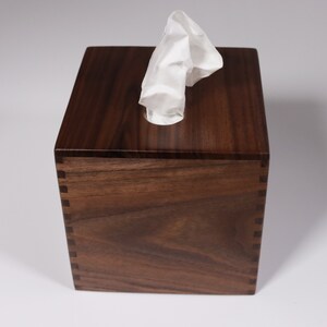 May include: A dark brown wooden tissue box with a white tissue peeking out of the opening.