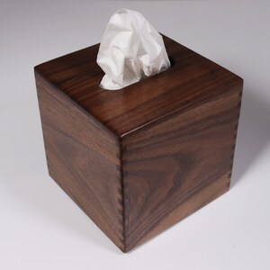May include: A dark brown wooden tissue box cover with a white tissue peeking out of the top opening.