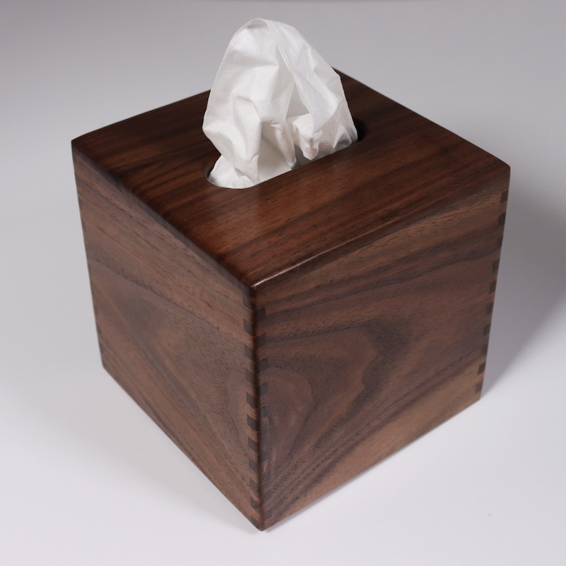 May include: A dark brown wooden tissue box cover with a white tissue peeking out of the top opening.