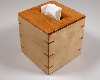 May include: A wooden tissue box cover made of maple wood with a cherry wood trim. The box has a square shape and a simple design.
