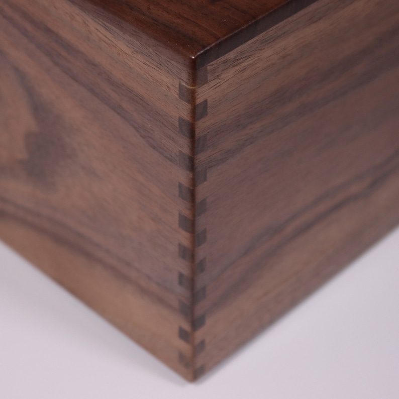 May include: Close-up of a wooden box with a dark brown finish. The box has a mitered corner with a visible dovetail joint.