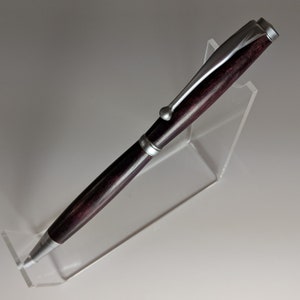May include: A silver and dark wood pen with a twist top. The pen is displayed on a clear acrylic stand.