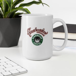 May include: White ceramic coffee mug with a large handle. The mug features the text "Frackuccino" in red and white script above a green and white logo that says "Starbucks Coffee". The mug is on a white surface.
