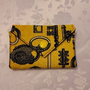 May include: A yellow fabric wallet with a black and white key design. The wallet has a yellow button.
