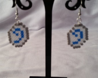 May include: A pair of silver earrings with blue and gray pixelated designs. The earrings are displayed on a black earring stand.