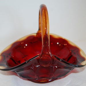 May include: A red glass basket with a clear amber handle. The basket has a scalloped edge and a textured design.