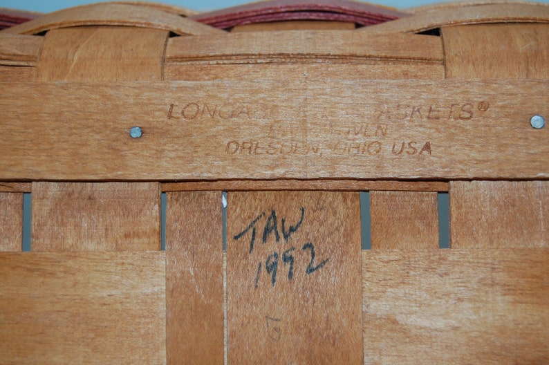 May include: Close-up of a wooden basket with a label that reads "Longaberger Basket Co. Dresden, Ohio USA". The basket is marked with the date "1972".