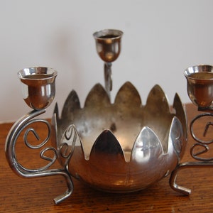 May include: Silver candle holder with three candle cups and a decorative bowl in the center. The candle holder has a floral design.