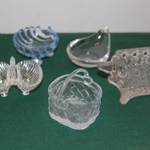 May include: Five small glass dishes in various shapes, including a shell, a basket, an anvil, and a leaf. The dishes are clear glass with intricate designs.