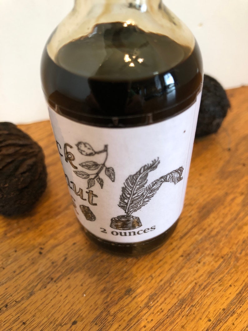 May include: A clear glass bottle filled with a dark liquid, labeled "Black Walnut" with botanical illustrations and a quill pen. The label indicates a 2-ounce volume. Two black walnuts are visible on a wooden surface.
