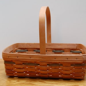 May include: A natural woven basket with a wooden handle. The basket is rectangular and has a light brown color.
