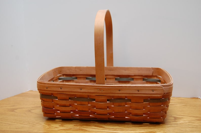 May include: A natural woven basket with a wooden handle. The basket is rectangular and has a light brown color.