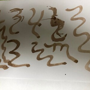 May include: Abstract brown ink strokes on white paper. The image features a series of free-flowing, wavy lines and stylized shapes, creating a dynamic and expressive composition. The ink varies in thickness, adding depth and visual interest to the artwork.