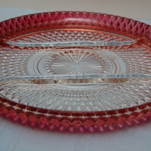 May include: A clear, divided serving dish with a ruby red rim. The dish has a diamond-cut pattern and a central starburst design. The dish is likely made of glass and is suitable for serving appetizers or snacks.