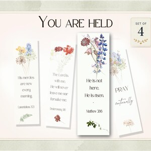 Puede incluir: Un conjunto de cuatro marcadores florales con citas inspiradoras. Cada marcador presenta ilustraciones de flores en acuarela y textos bíblicos. Las palabras "You Are Held" están en la parte superior, y el conjunto incluye una pequeña tarjeta "Set of 4".