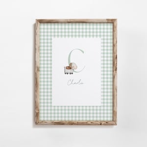 Può includere: Opera d'arte incorniciata con uno sfondo a motivo gingham verde chiaro. L'opera include un'illustrazione ad acquerello di un cane, la lettera "C" e il nome "Charlu" in corsivo. La cornice è in legno.
