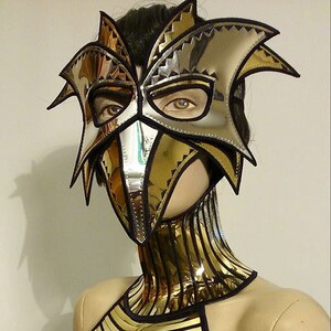 May include: A gold and silver metallic mask with a bird-like design. The mask is worn by a mannequin with a gold and black metallic bodice.