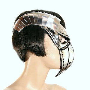 May include: A silver and black masquerade mask with a geometric design. The mask has a pointed chin and a large, open eye area.