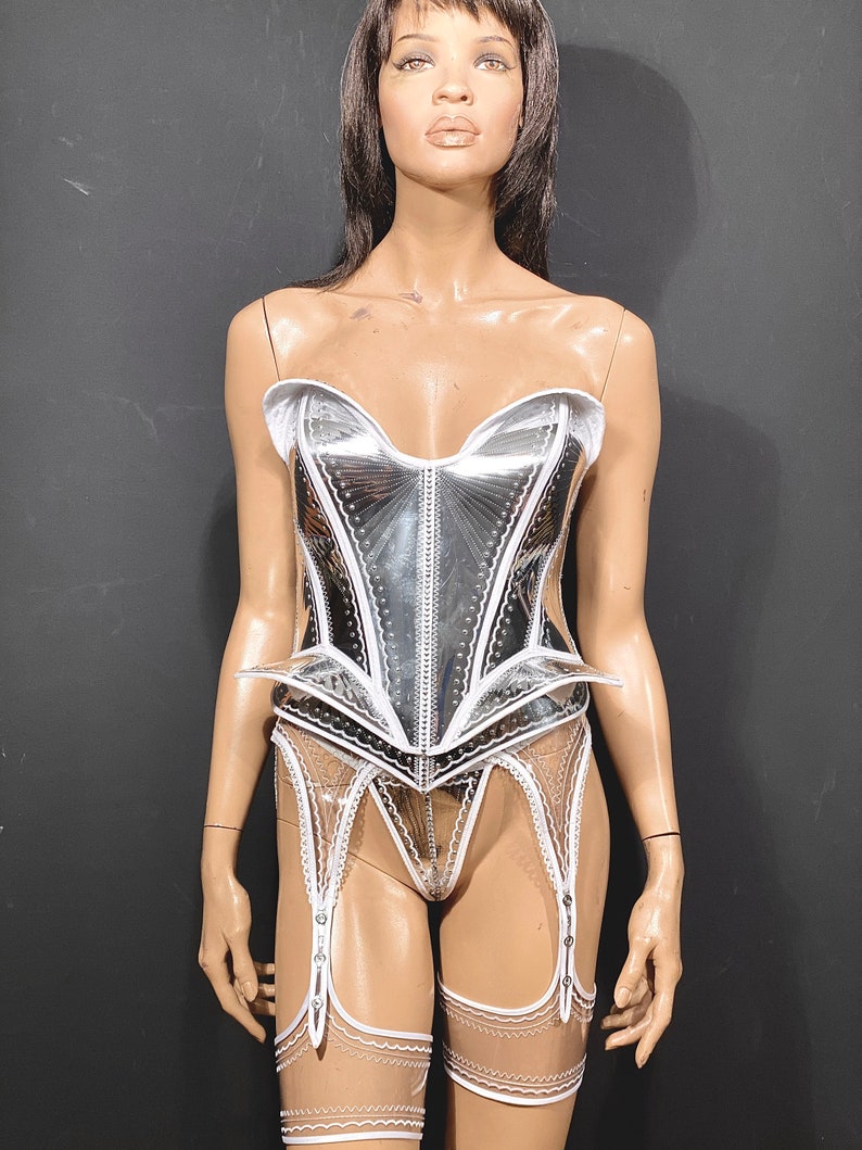 May include: A silver and white corset with a lace trim and a matching garter belt. The corset has a sweetheart neckline and a boned construction.
