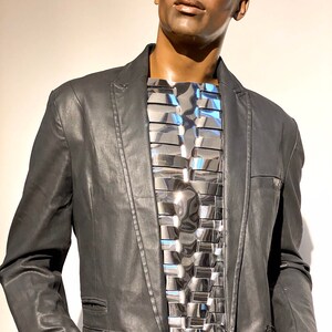Pu&ograve; includere: Un blazer nero con un pezzo di petto in metallo argentato. Il pezzo di petto &egrave; composto da molti piccoli pezzi rettangolari disposti a griglia.