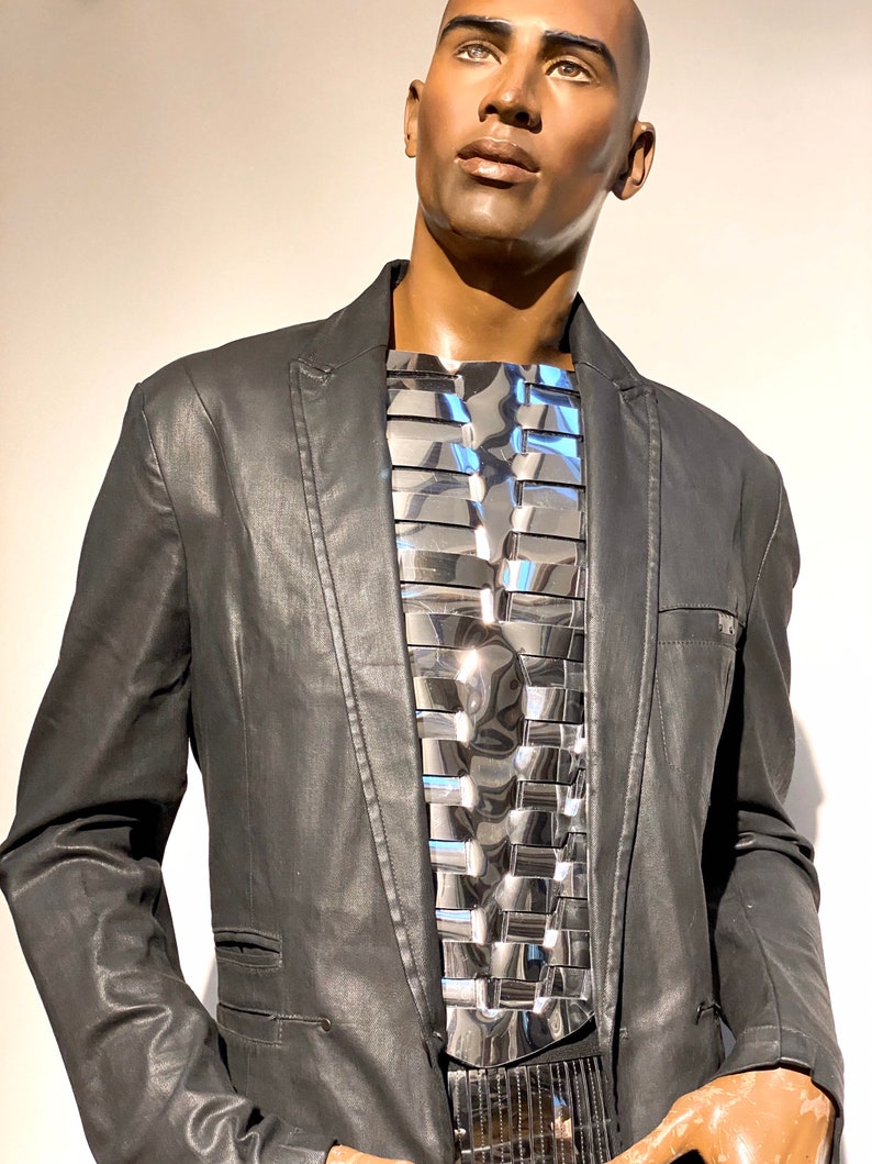 Pu&ograve; includere: Un blazer nero con un pezzo di petto in metallo argentato. Il pezzo di petto &egrave; composto da molti piccoli pezzi rettangolari disposti a griglia.