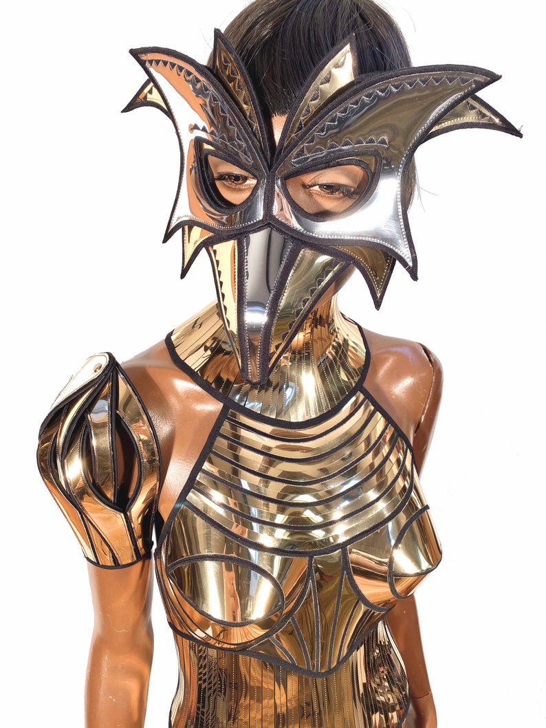 May include: A silver and black metallic costume with a bird-like mask. The costume features a geometric design with a high neckline and a fitted bodice.