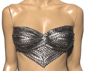 May include: A silver-colored, woven, strapless bra with a pointed bottom edge. The bra is worn by a mannequin with short black hair.
